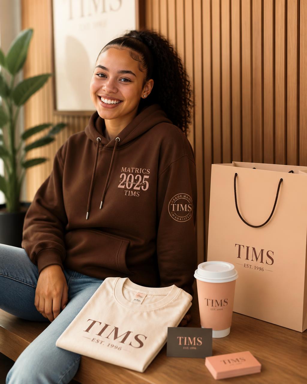 Student wearing a custom TIMS matric hoodie with branded apparel, business cards, coffee cup and shopping bag